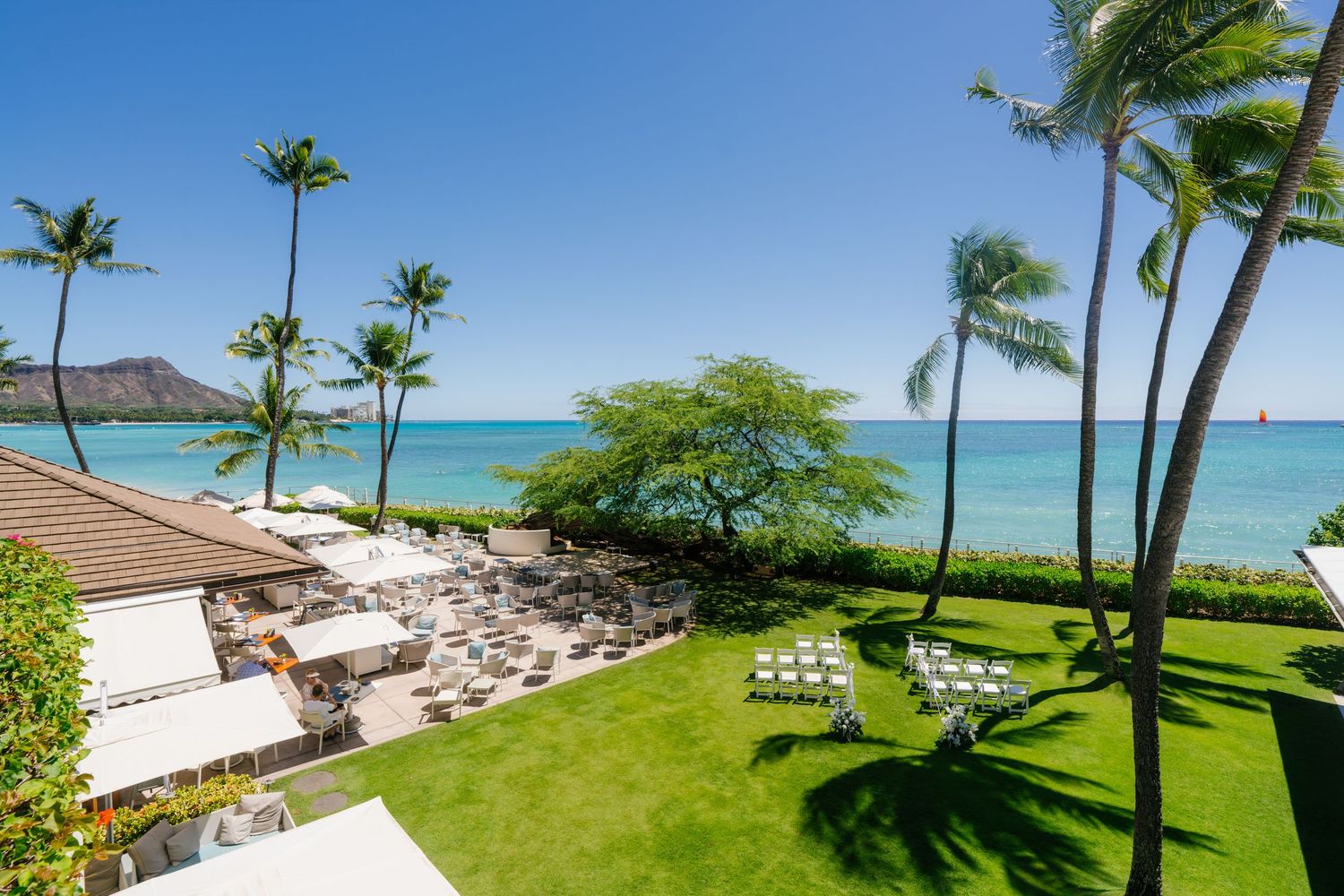 Tropical beachfront resort with palm trees, white lounge chairs, lush lawn, and Diamond Head views in Halekulani Hotel.
ハレクラニホテルウェディング
