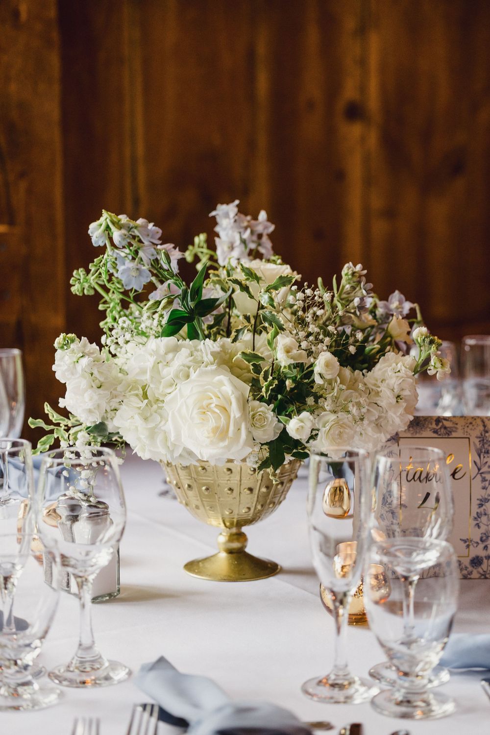 Elegant white floral centerpieces with roses and greenery arranged on tables with crystal glassware at a wedding reception.