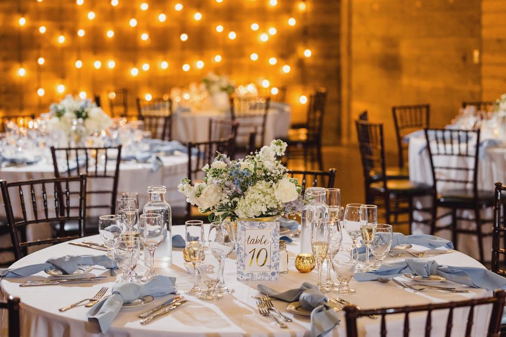 Elegant wedding reception table setting with white floral centerpiece and string lights overhead.