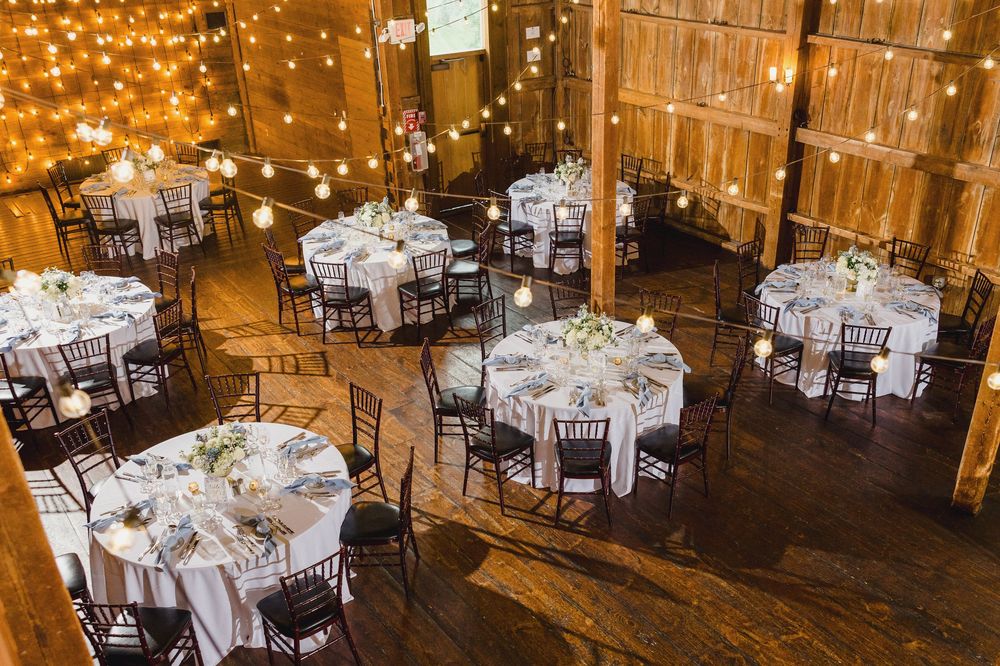 Elegant barn reception setup with round tables and warm string light ambiance.