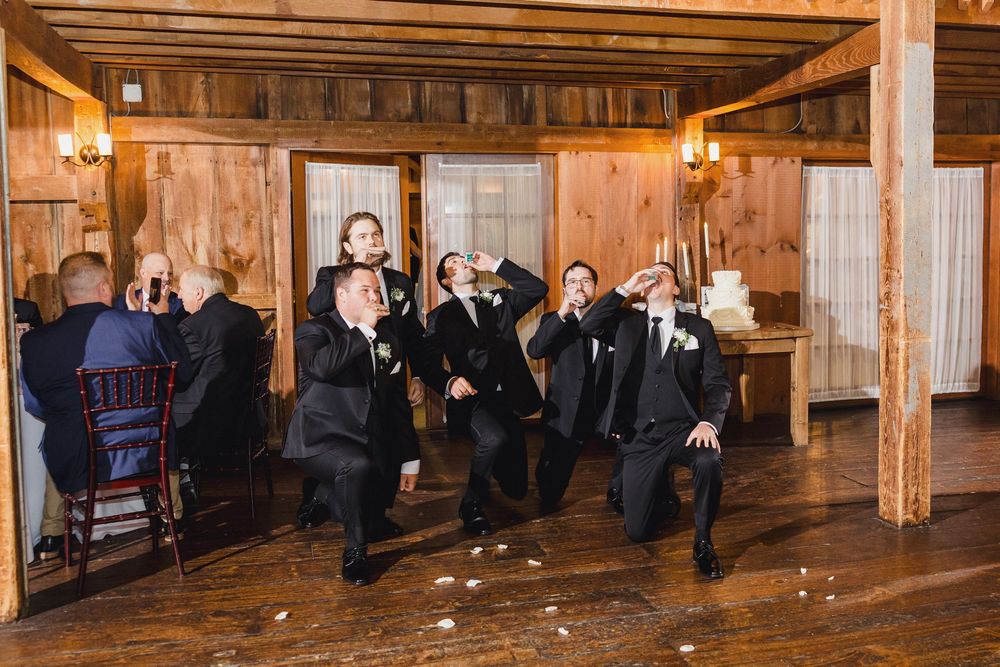 A panoramic view of a rustic barn wedding venue with wooden beams and string lights.