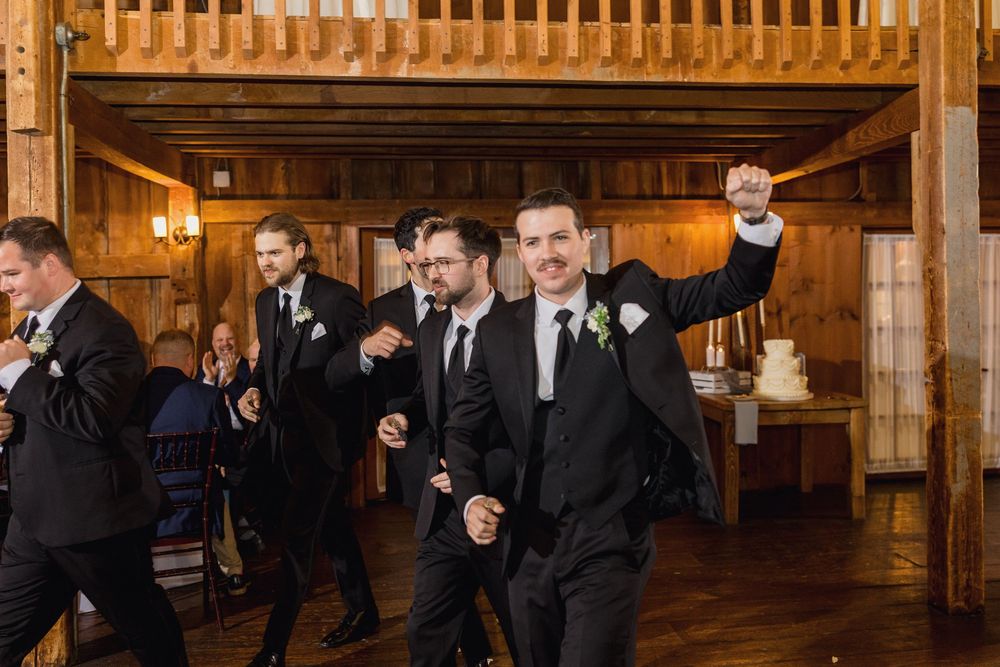 Wedding guests in formal attire gather inside a spacious wooden barn reception venue.