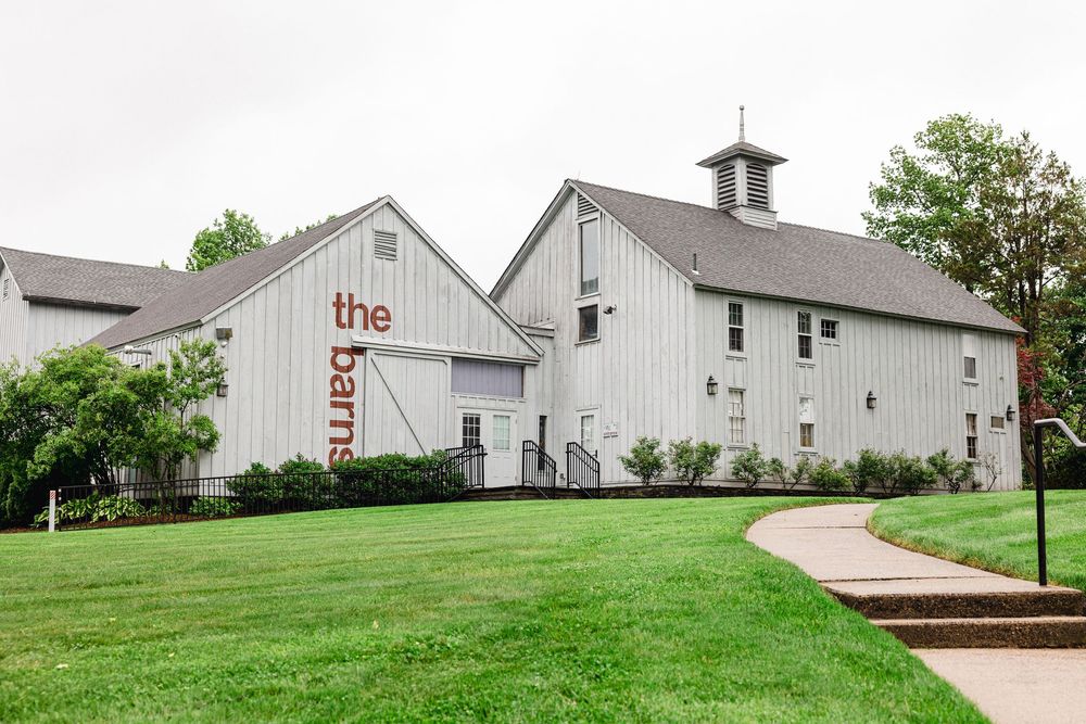 A white barn-style wedding venue with classic architecture sits on a manicured green lawn.