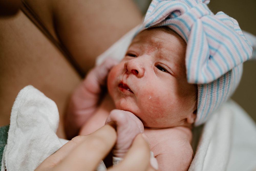 A newborn baby wearing a blue and white striped hat rests peacefully in a hospital setting.
