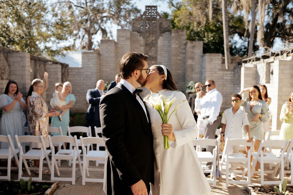 Romantic wedding ceremony in front of a stone wall backdrop with guests seated on white chairs.