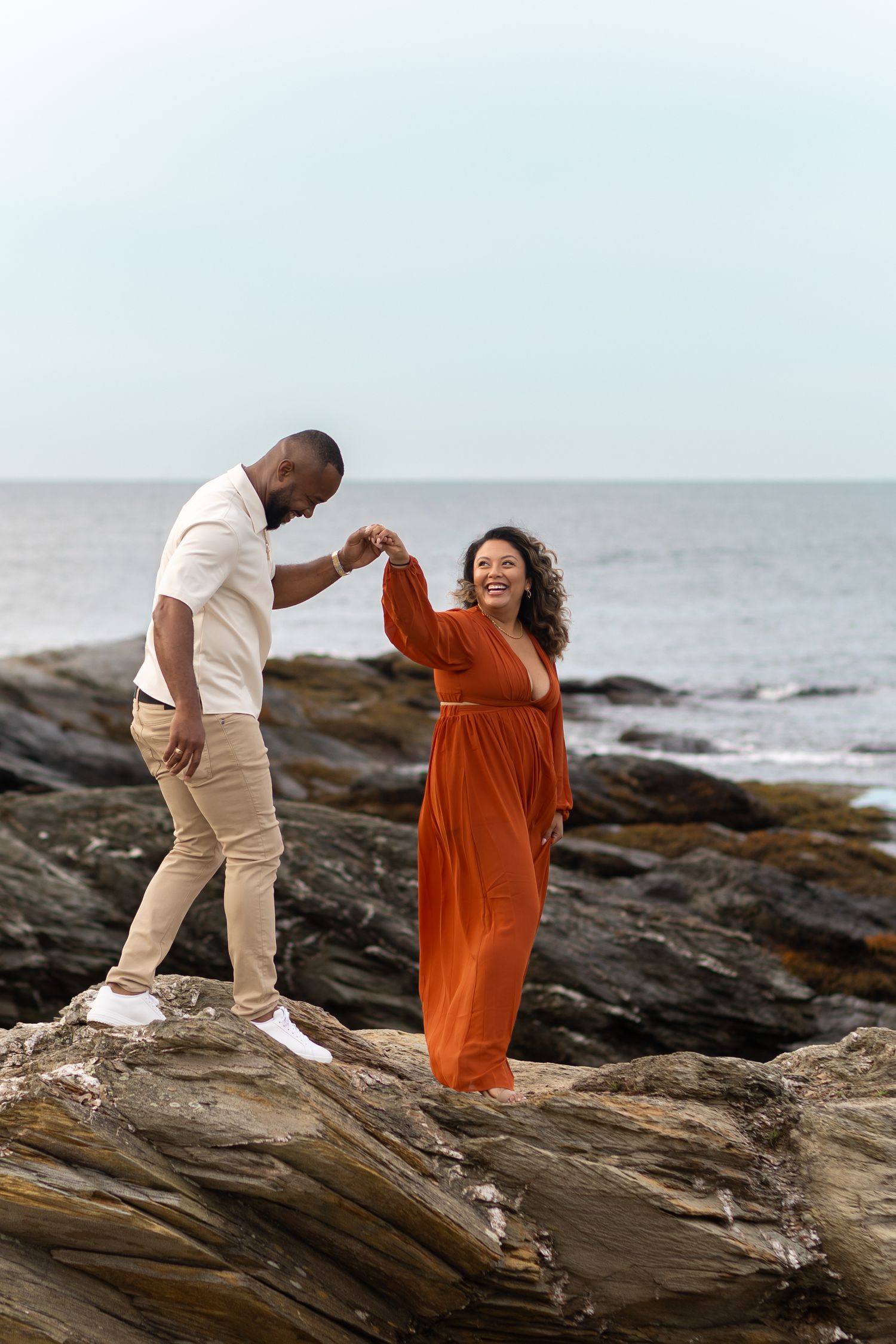 A couple share a romantic moment on rocky coastal cliffs by the ocean at sunset in Beavertail State Park, Jamestown, RI.
