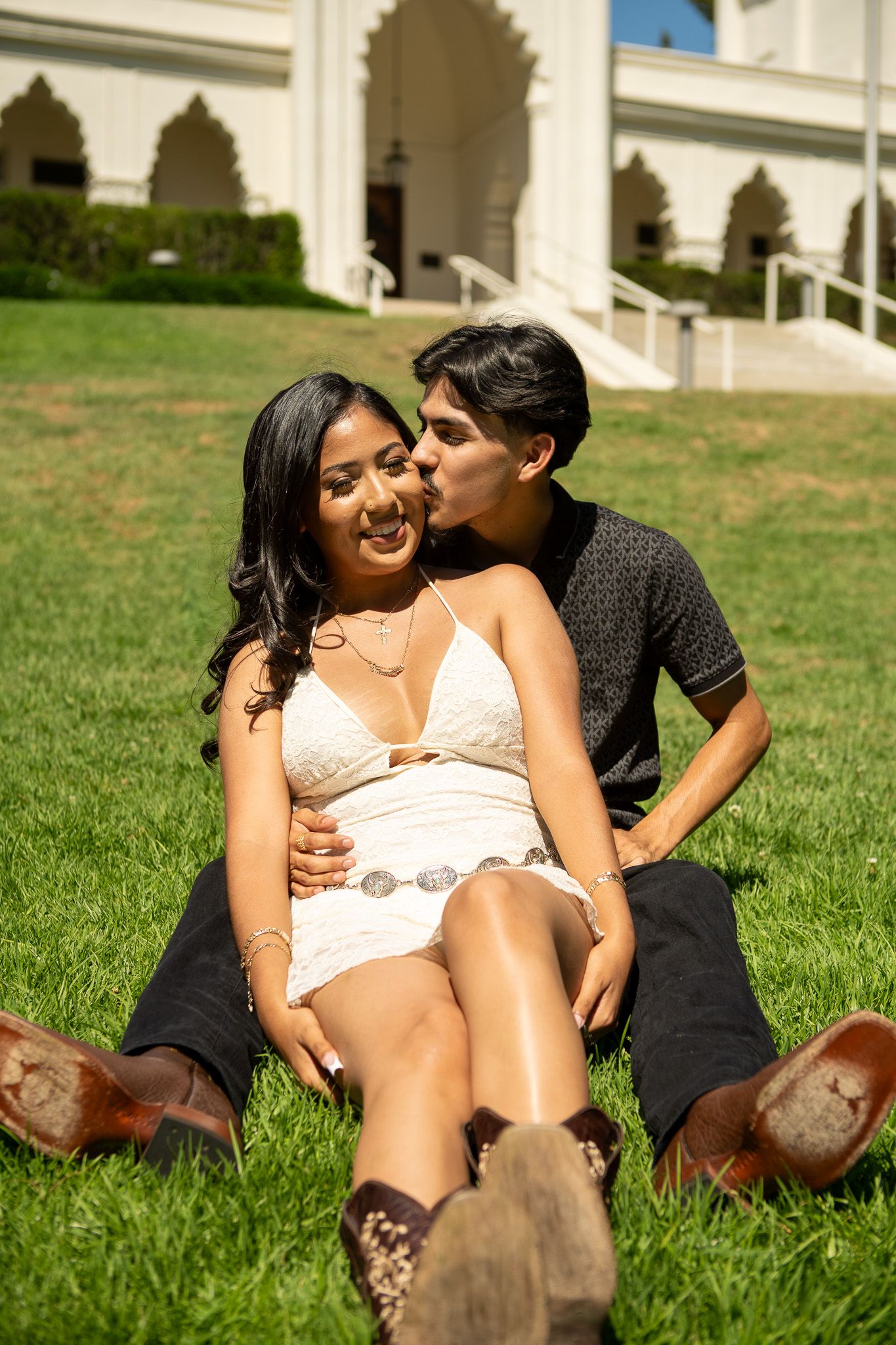 A couple shares an intimate moment while relaxing together on green grass on a sunny day.