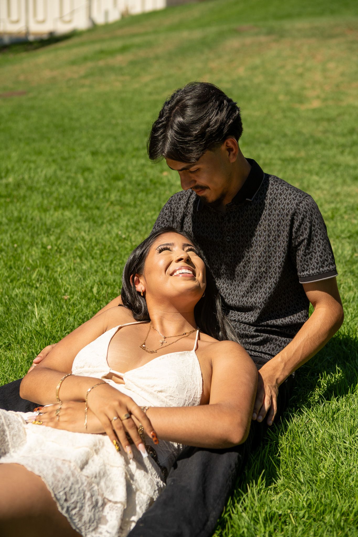 A couple relaxes together on lush green grass in a romantic outdoor photoshoot series.
