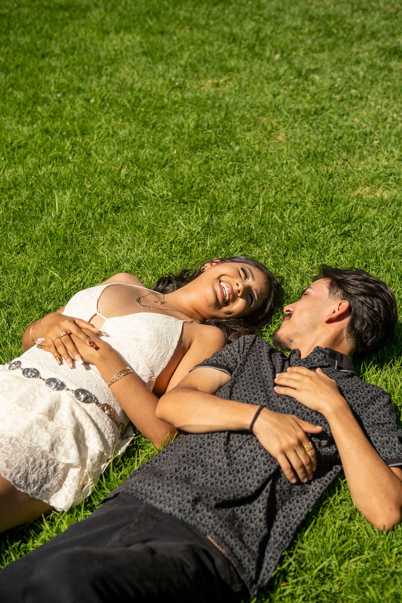 A couple lies together on green grass, sharing a tender moment in a romantic outdoor setting.
