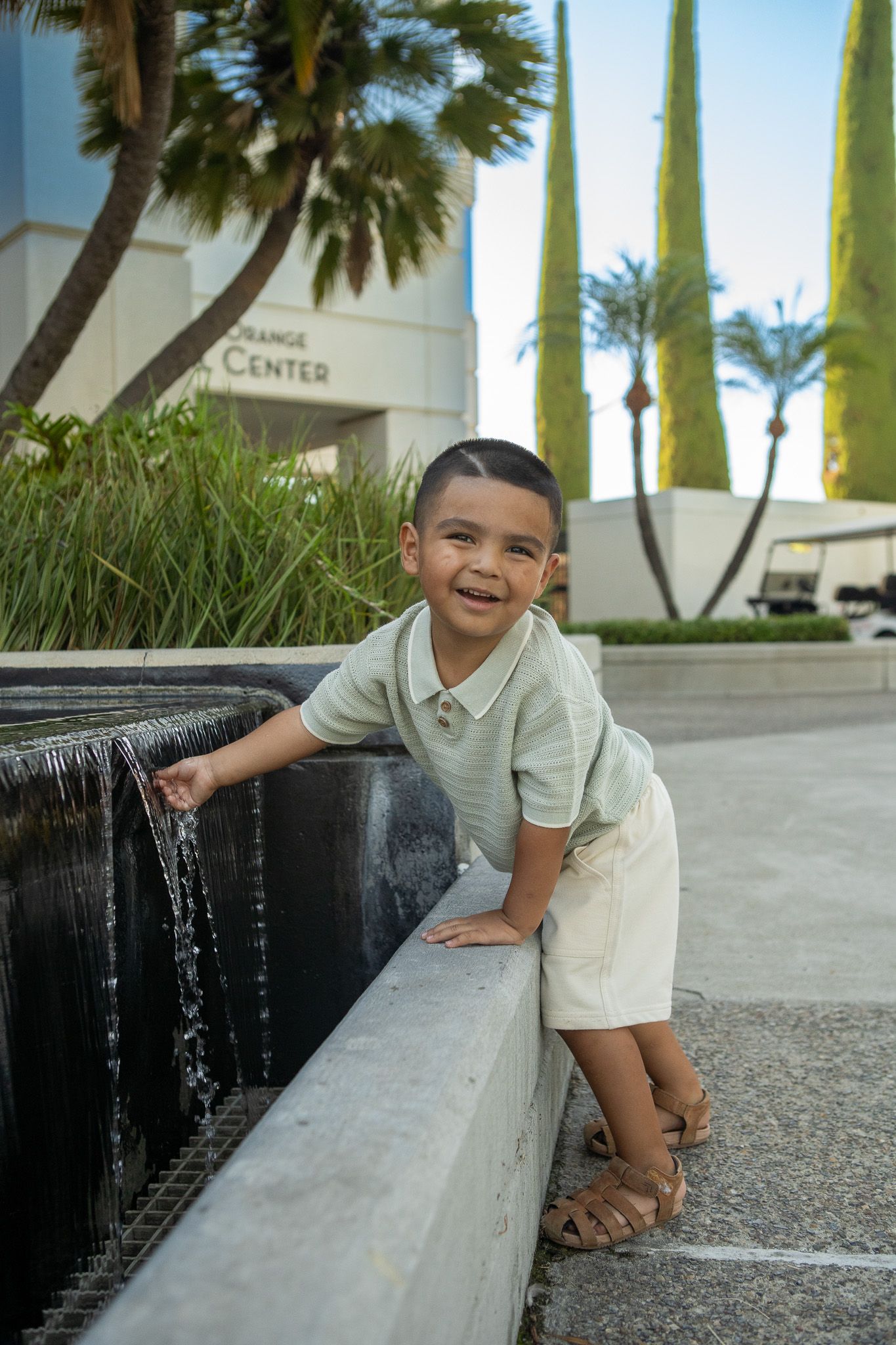 A young child plays and smiles while exploring a water feature with cascading fountains at an outdoor plaza.