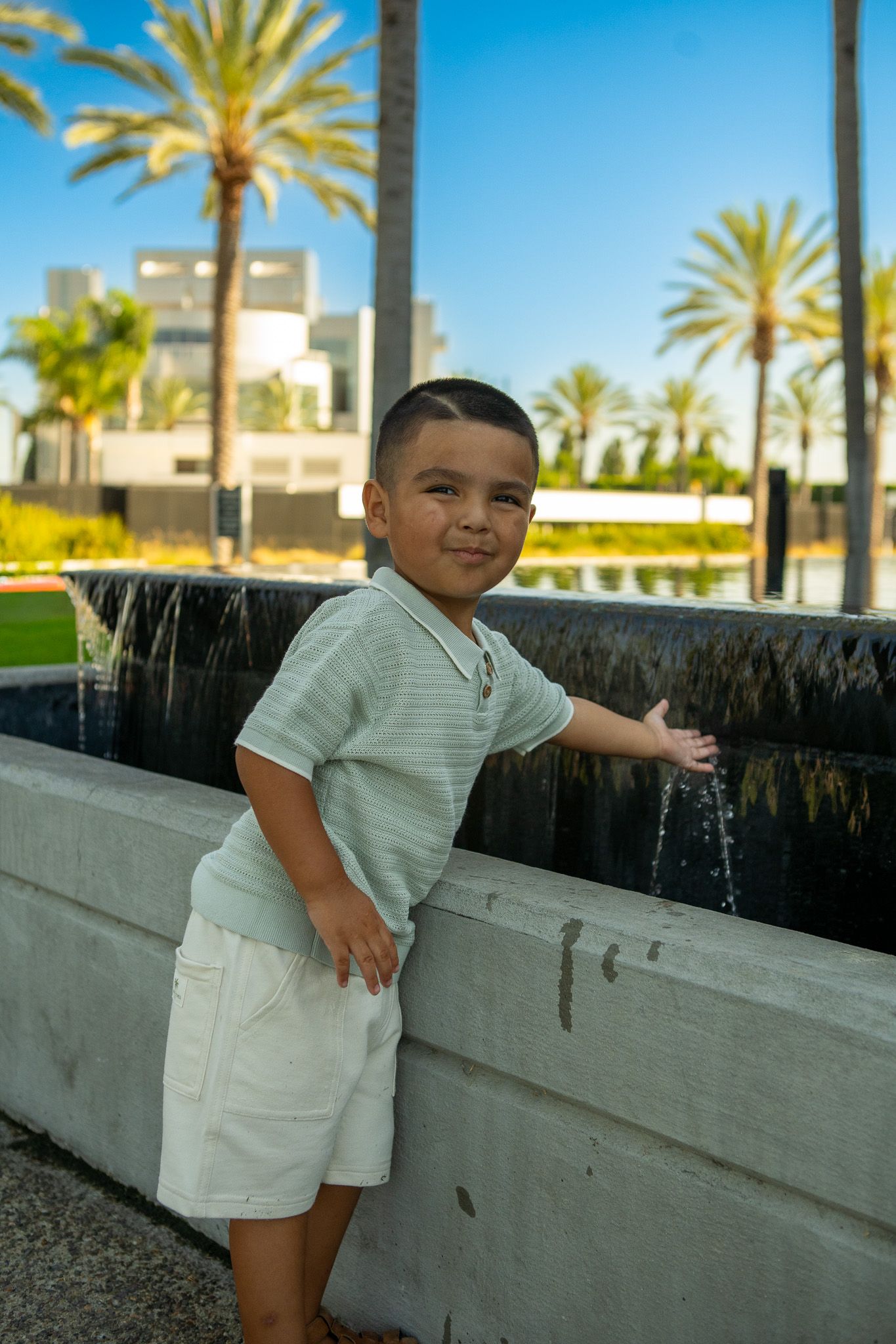 A young child in white clothing plays near a concrete wall with palm trees visible in the background at a resort.