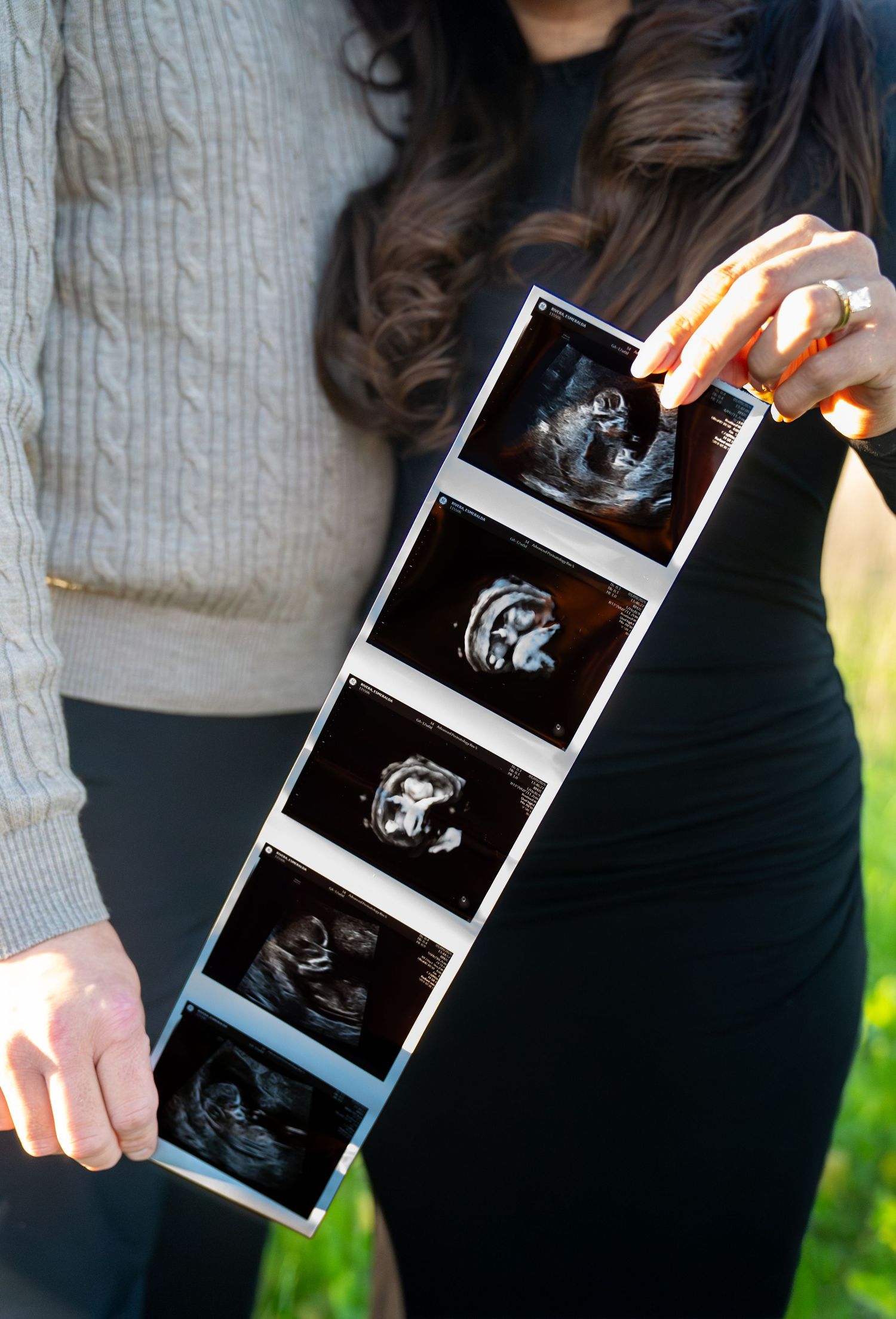 A couple holding ultrasound photos outdoors while sharing a special pregnancy announcement moment.
