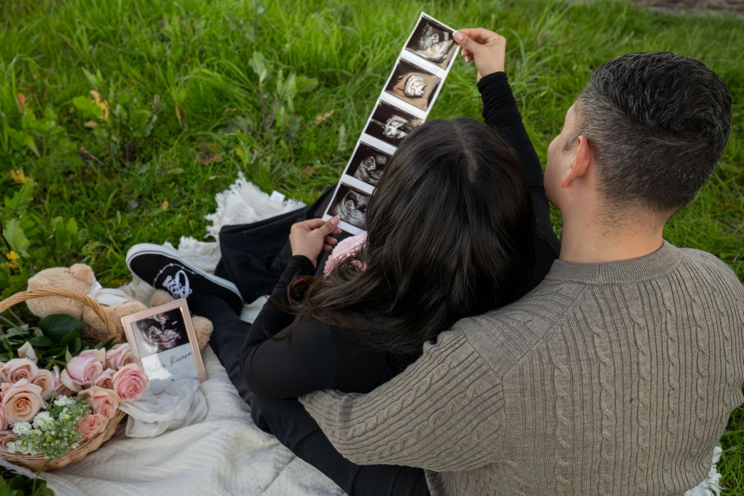 Person lying in grass looks at old photographs while relaxing outdoors on a sunny day.