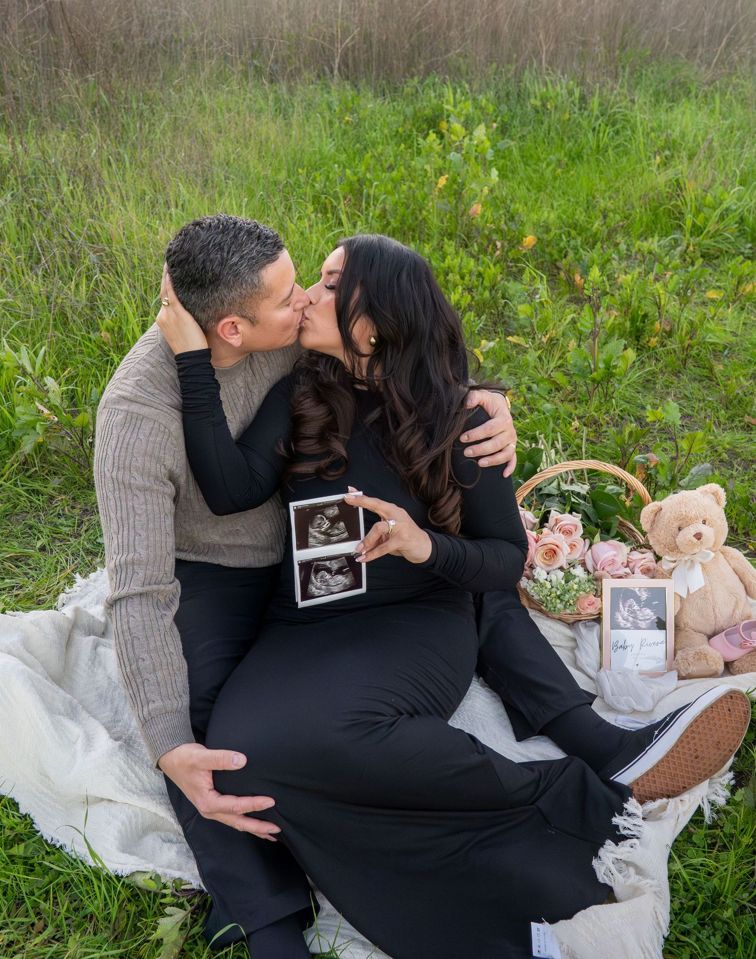 Intimate outdoor maternity photoshoot with couple sharing tender moments while holding ultrasound photos and teddy bear.