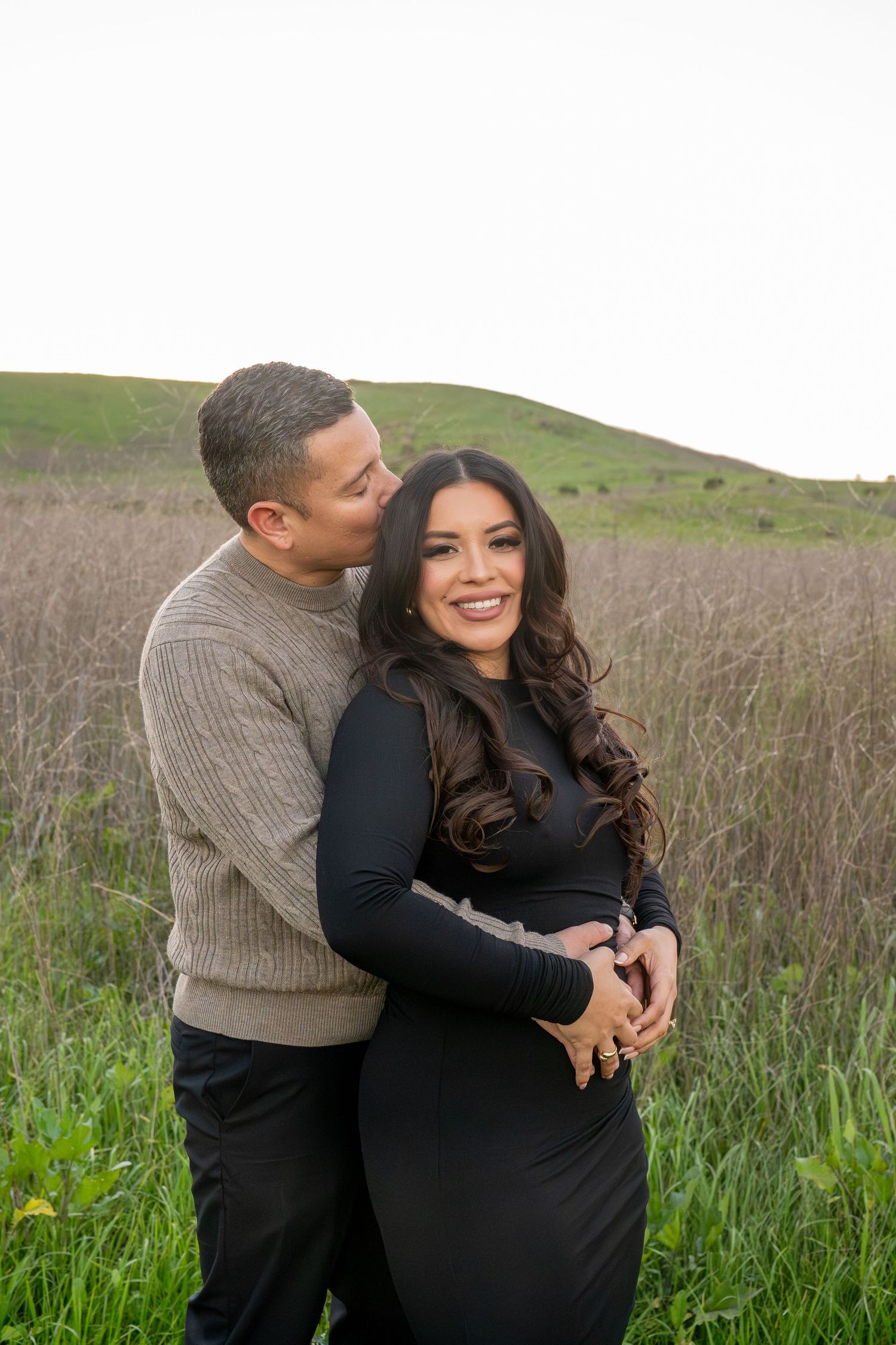 Couple embracing in a field of tall grass during sunset pregnancy photoshoot.