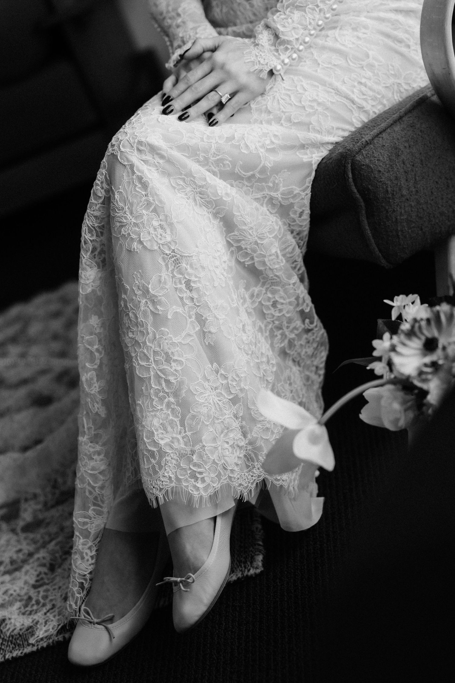 Black and white detail of a bride's lace wedding dress, hands, and floral bouquet during an intimate wedding moment.