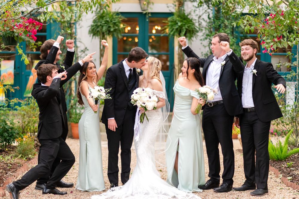 Wedding party celebrates joyfully in a lush garden setting with blooming flowers and greenery.