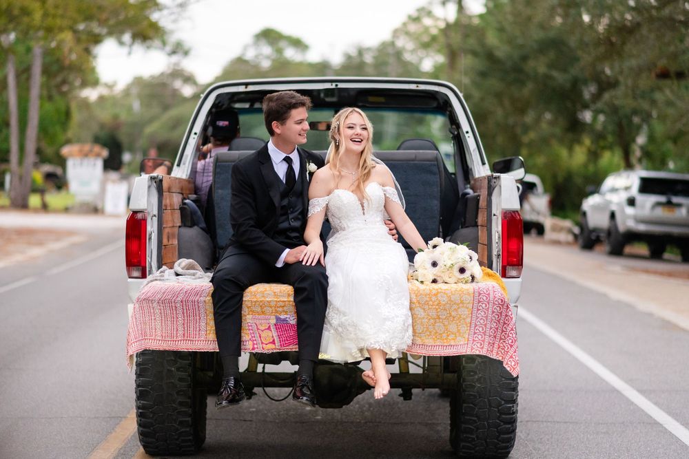 A newlywed couple sits in the back of a vintage pickup truck decorated for their wedding day.