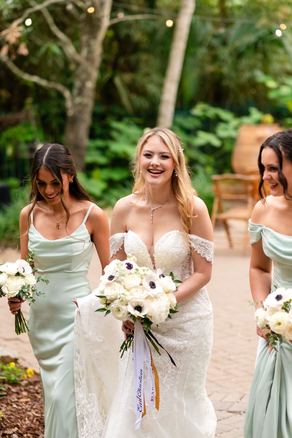 A bridal party poses with white and cream bouquets, bridesmaids wearing mint green silk dresses.