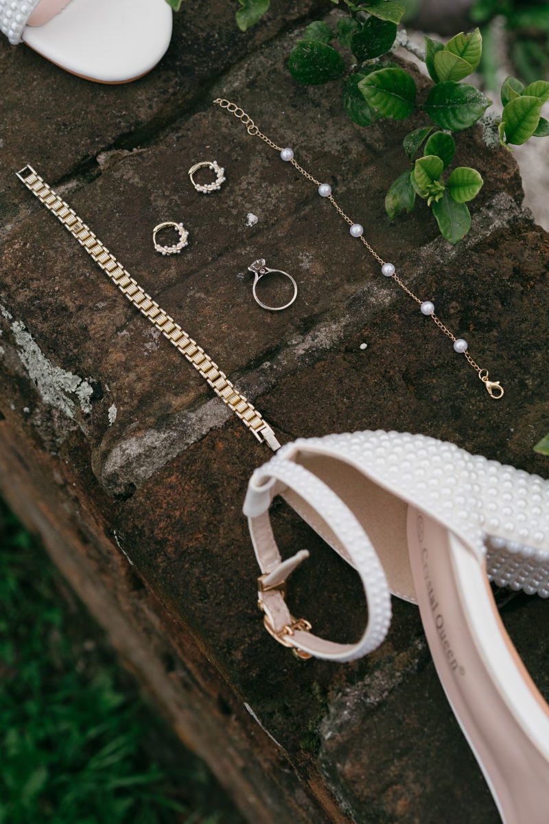 Elegant gold jewelry and accessories including a bracelet and ring arranged on a rustic stone surface with green foliage.