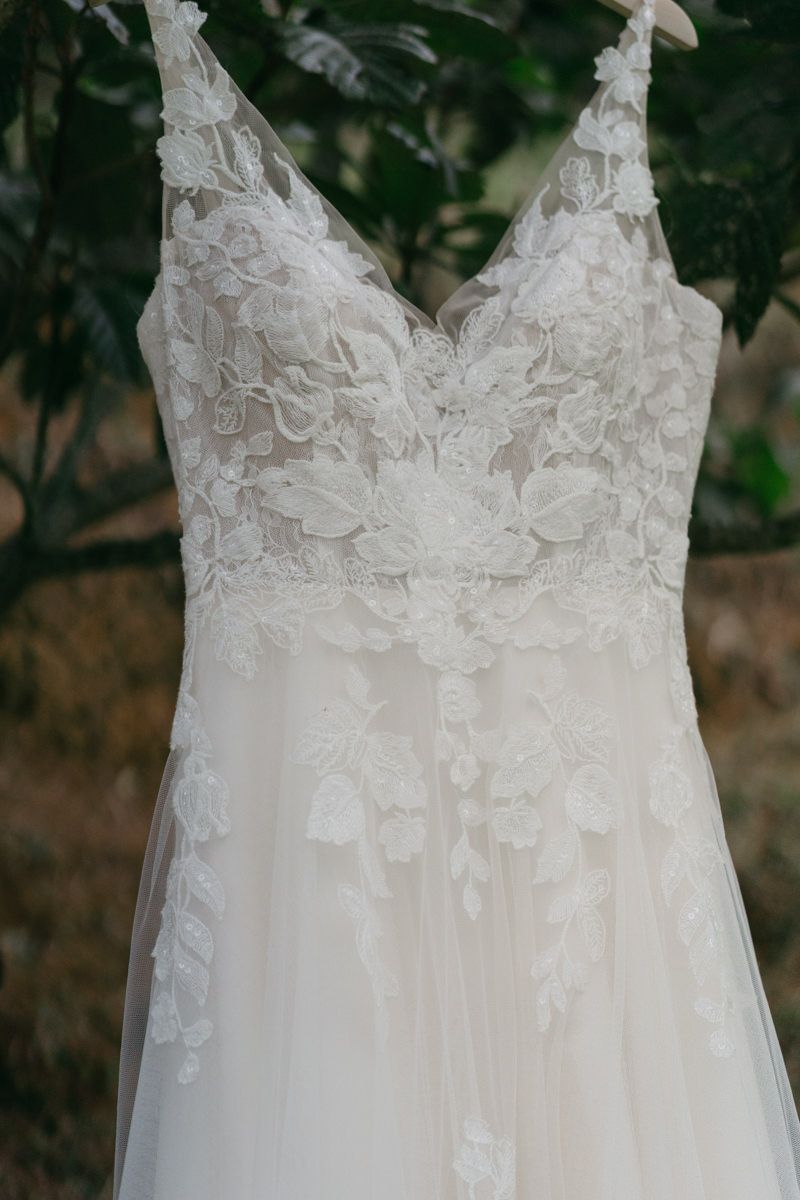 Close-up detail of white lace and tulle wedding dress bodice with delicate floral appliques and spaghetti straps.
