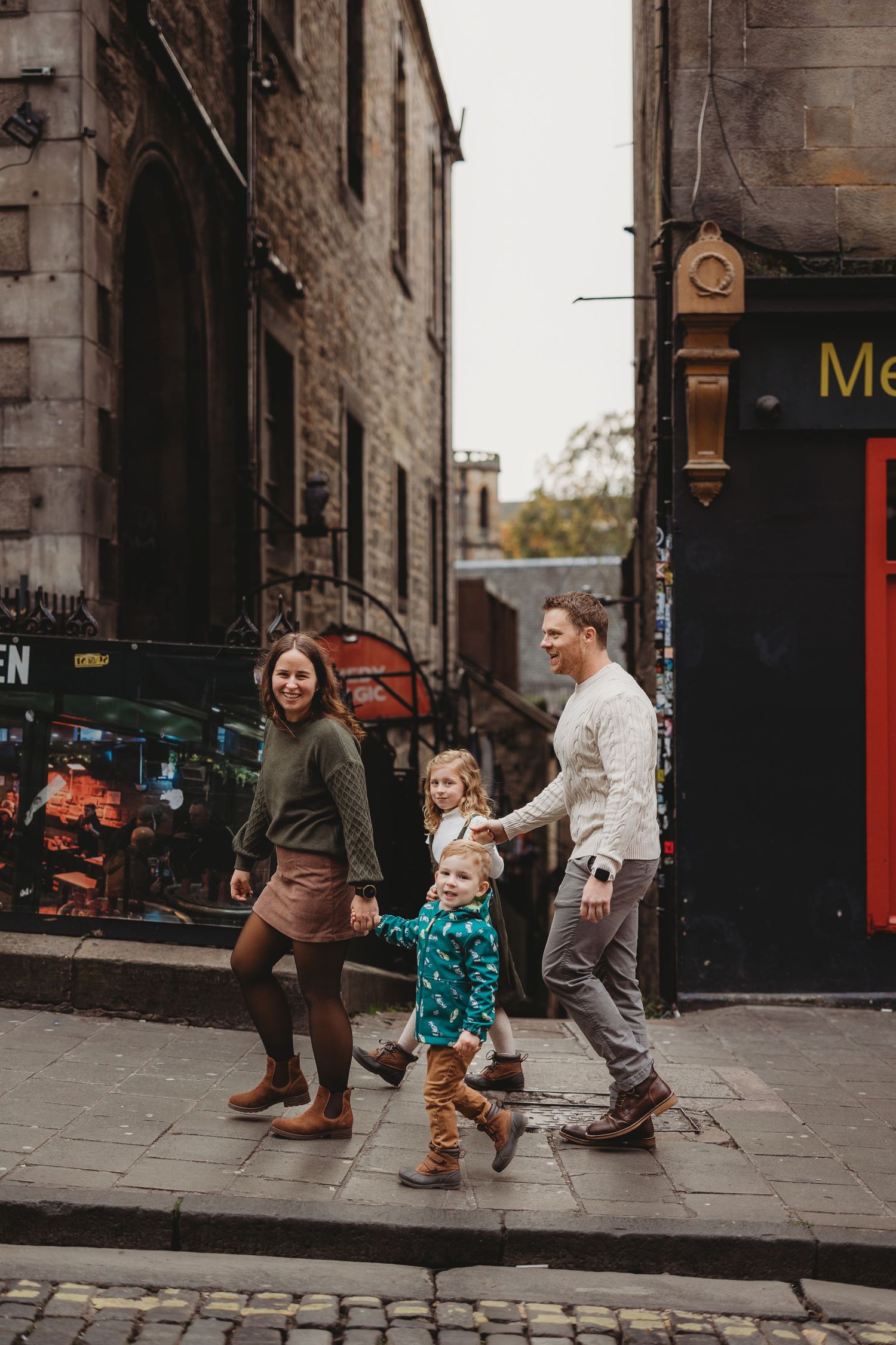 A family plays together on a historic cobblestone street in front of old stone buildings.