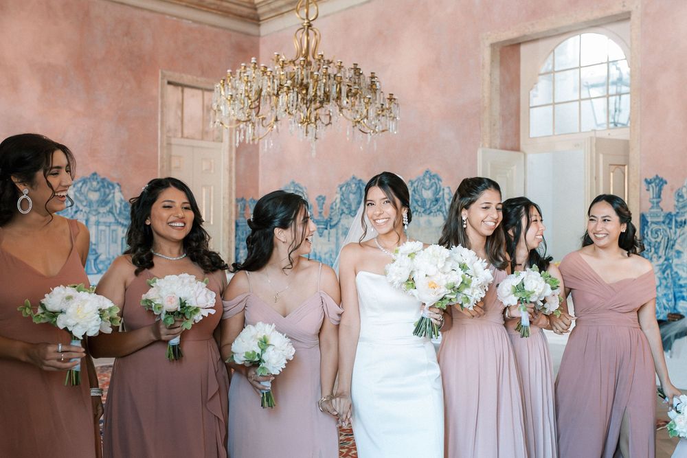 Bride with bridesmaids in blush dresses inside Palácio de Fronteira room with chandeliers and tiles