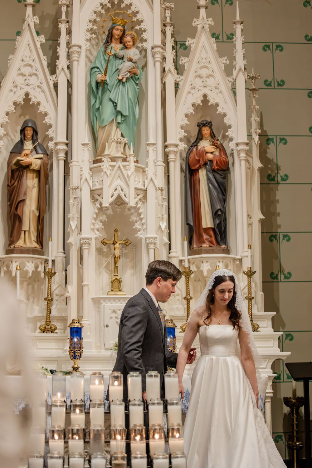 A couple stands at the altar in an ornate Catholic church with Gothic architecture and religious statues.