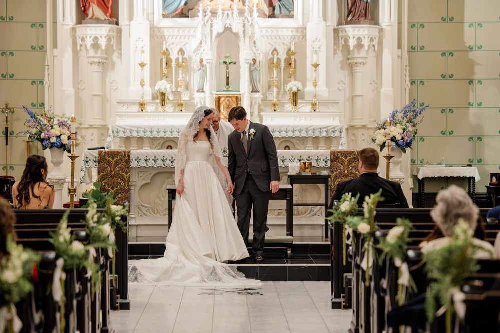 Interior of a Catholic church with ornate altar, white columns and floral decorations along the pews.