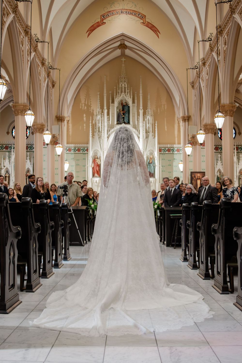 Elegant church wedding ceremony with long white train dress and guests seated in ornate cathedral pews.