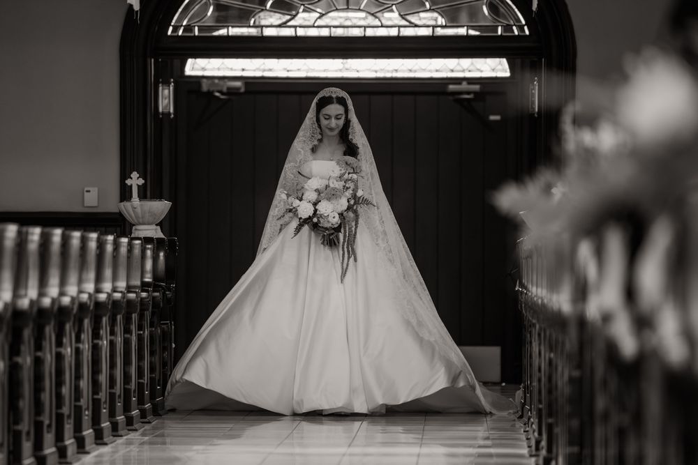 A bride in a white wedding gown stands elegantly at the top of a grand staircase in black and white photography.