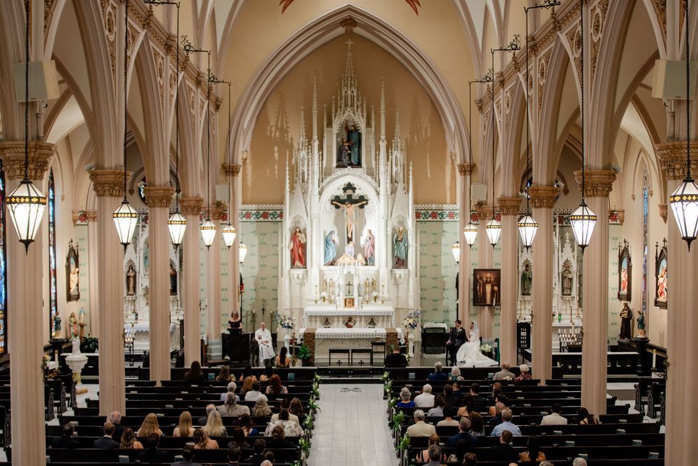 Gothic arched cathedral interior with rows of pews and ornate vaulted ceilings illuminated by hanging lights.