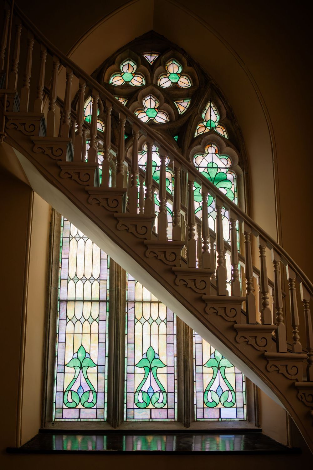 Beautiful stained glass windows with green accents line a wooden staircase in historic architecture.
