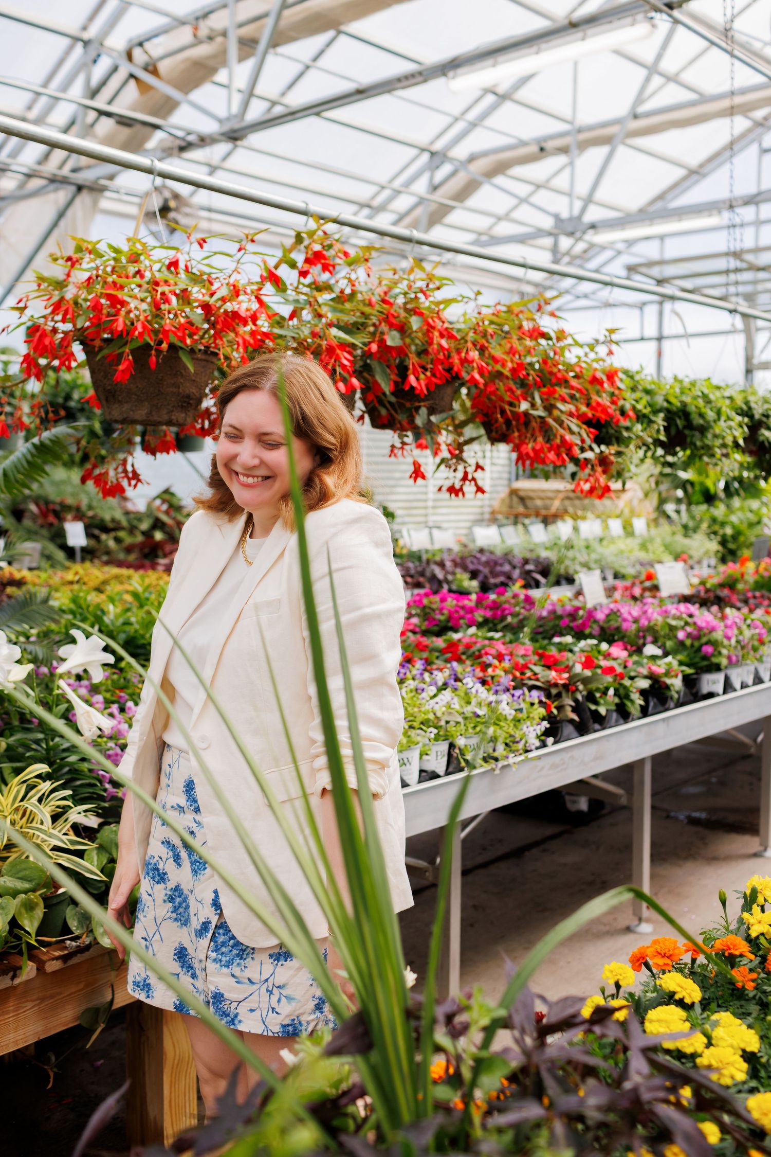 Shopper browses colorful flower displays in a sunny greenhouse filled with vibrant spring blooms and hanging baskets.