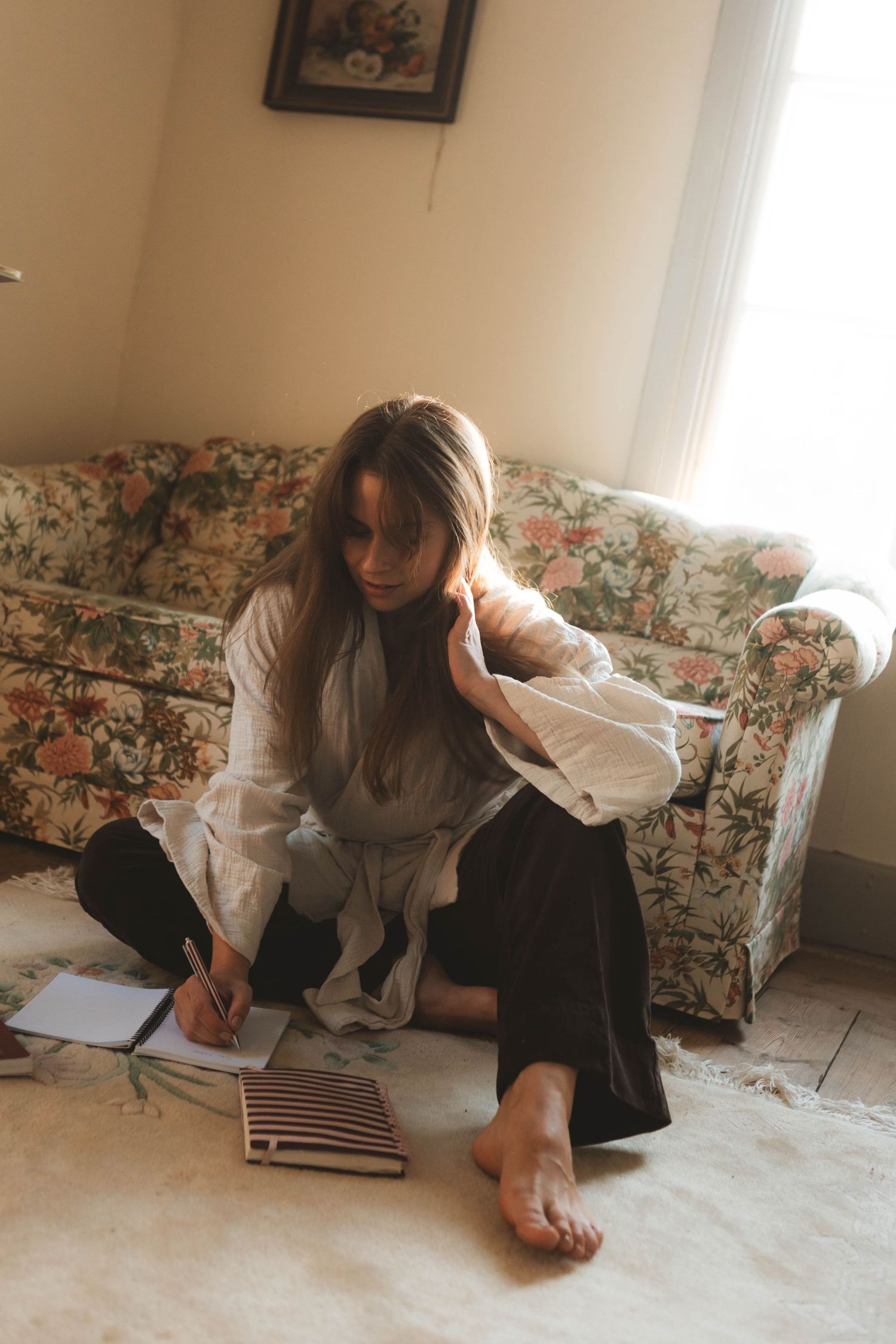 A person working on a laptop at an antique wooden table in a cozy sunlit room with vintage decor.