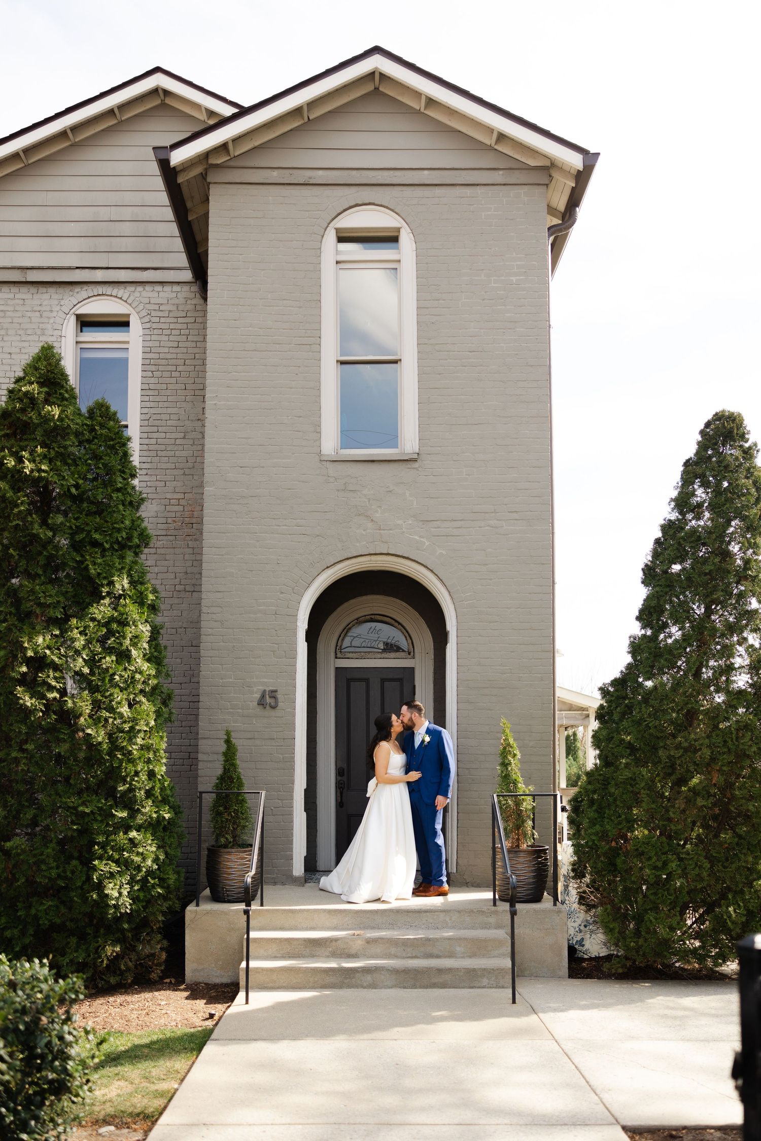 A couple stands at the entrance of a modern beige church building with arched doorway and symmetrical architecture.