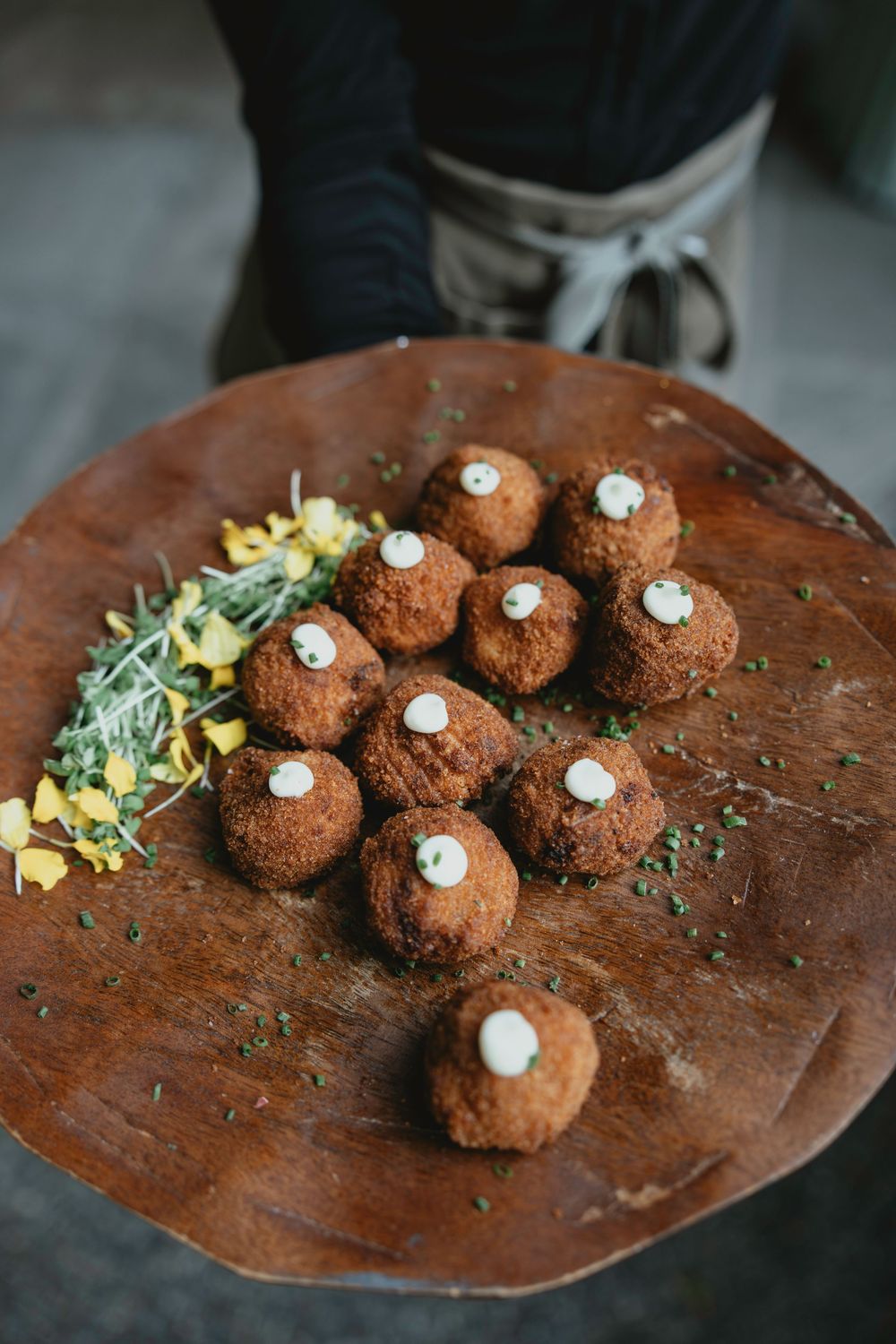 Chocolate truffles topped with white cream dots arranged on a rustic wooden serving plate with herb garnish.