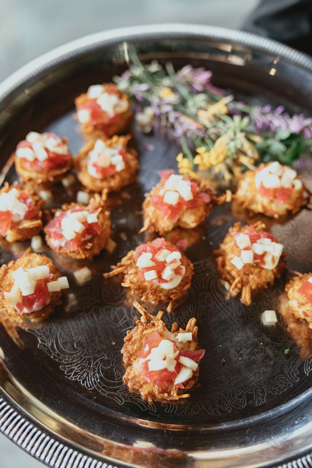 Crispy seafood crostini appetizers garnished with colorful toppings served on an ornate dark platter.