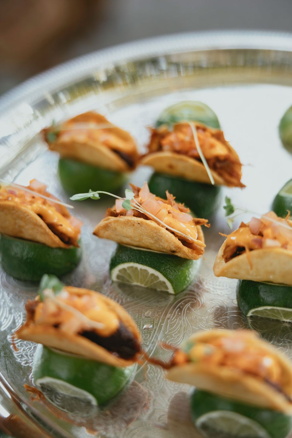Mini shrimp tacos served on a clear glass platter with fresh lime wedges and garnish.
