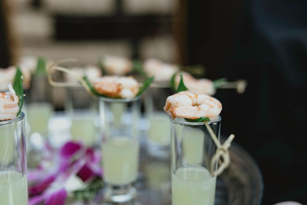 Elegant cocktail glasses filled with lime green drinks garnished with shrimp and fresh herbs on a party table.