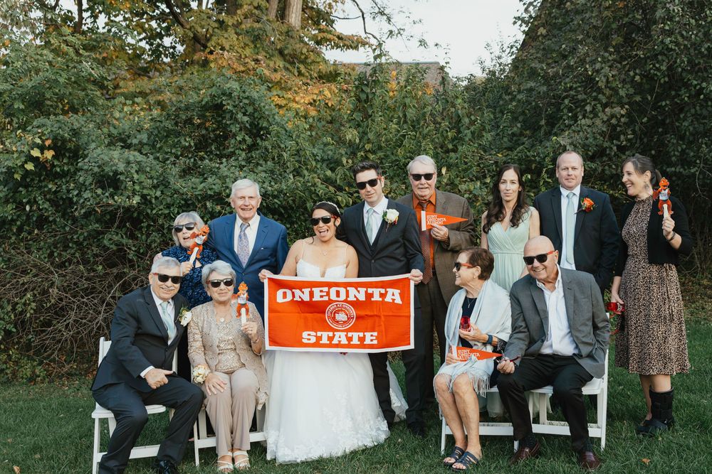 Wedding party poses together outdoors in front of orange state park sign during autumn celebration.