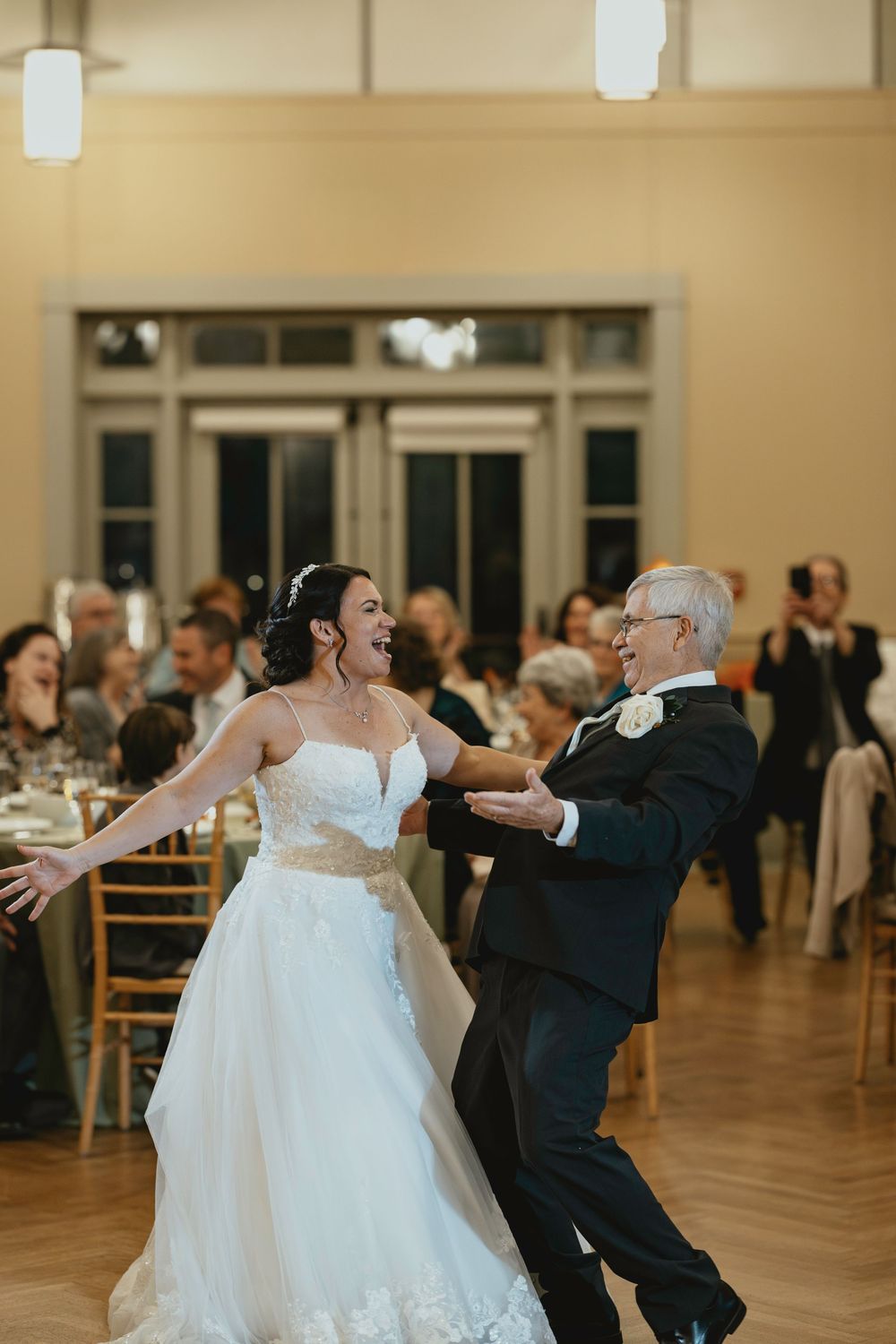 Couples dancing in a grand ballroom with elegant decor and hardwood floors during a wedding reception celebration.