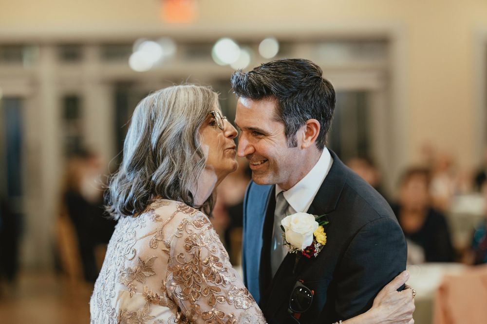 A couple sharing an intimate dance moment at a wedding reception with guests in the background.
