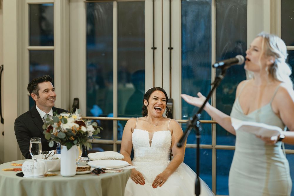 Wedding reception guests dancing and celebrating together in an elegant venue with large windows.