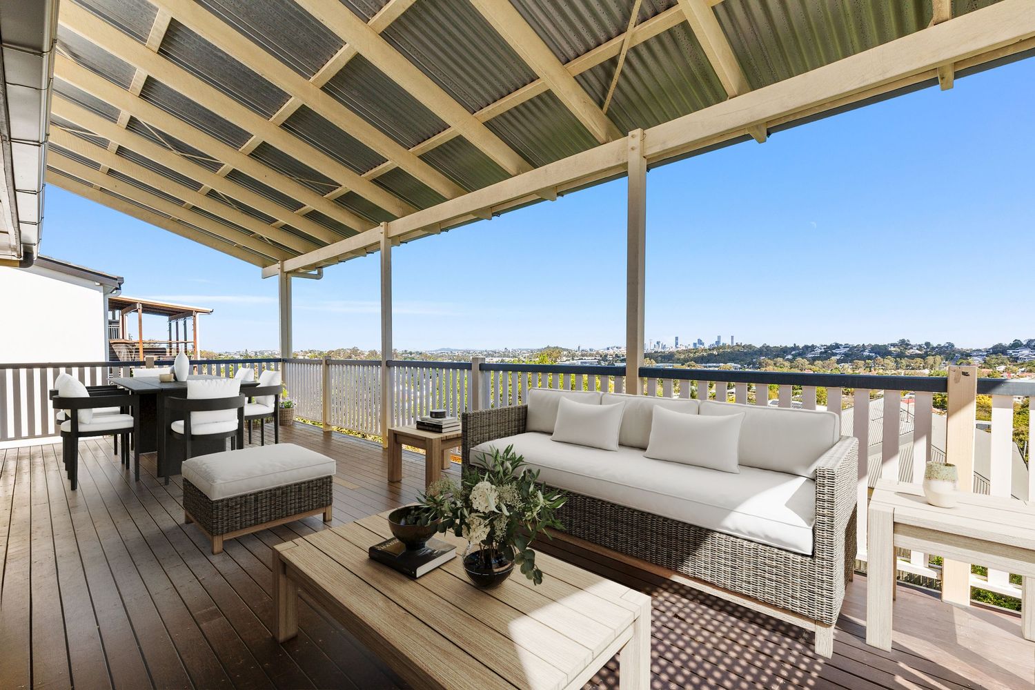Covered outdoor deck with wicker sofa, dining setting, and panoramic views of surrounding landscape.