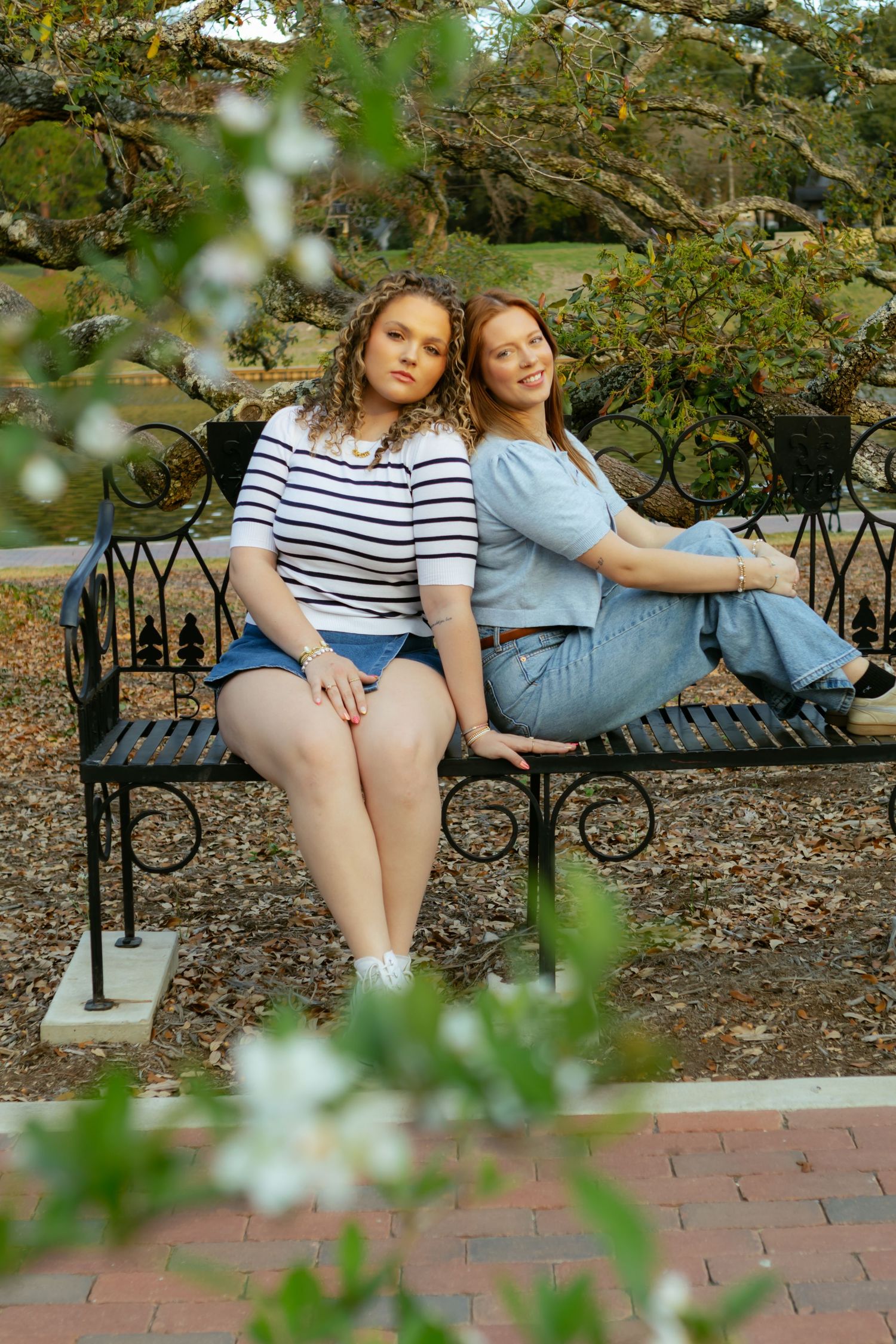 Two friends relax together on a decorative metal bench in a garden setting with brick pathways and greenery.