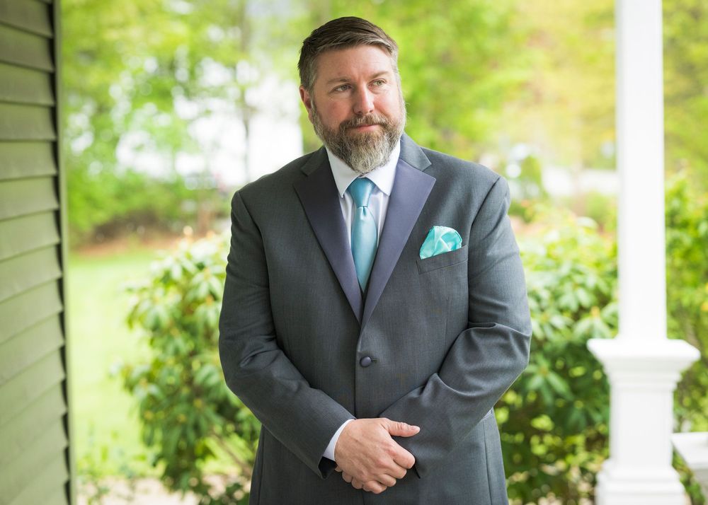 Bearded groom in gray suit with teal tie and pocket square posing outdoors.