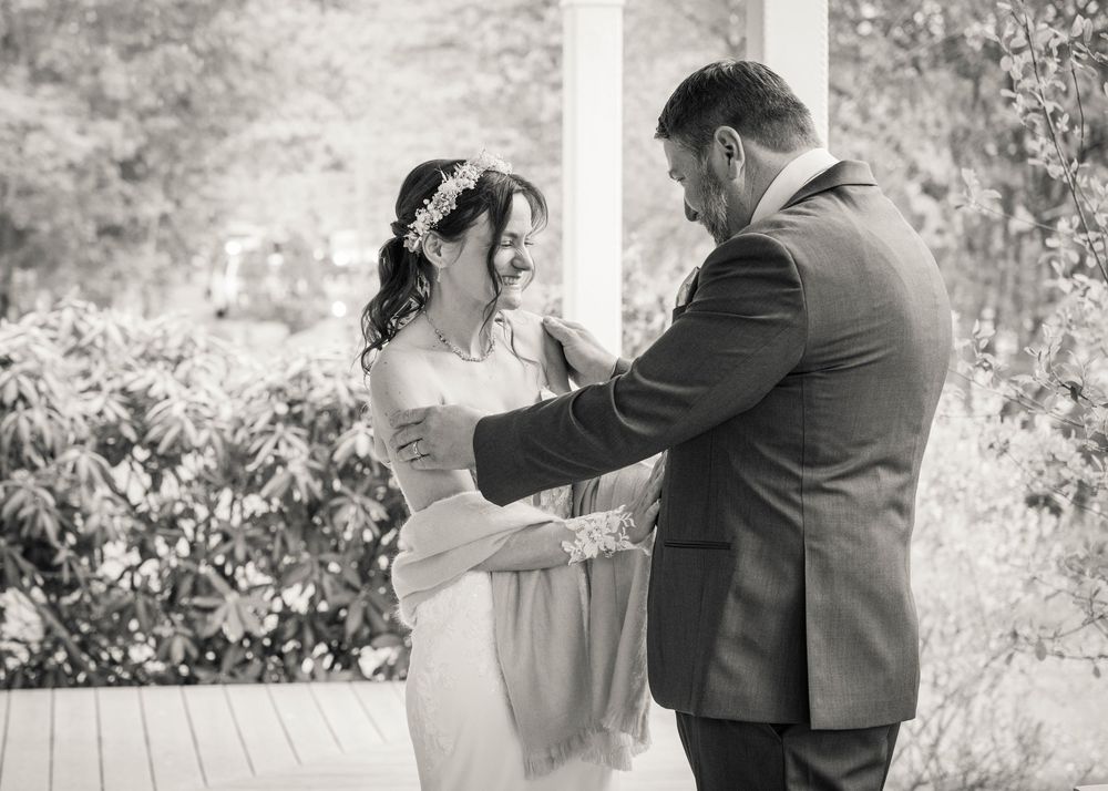 Black and white photo of a bride and groom sharing a tender moment on a porch during their wedding ceremony.