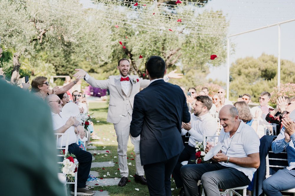 Ingresso dello sposo tra applausi e petali rossi durante la cerimonia nel giardino di Villa Casa Rossa