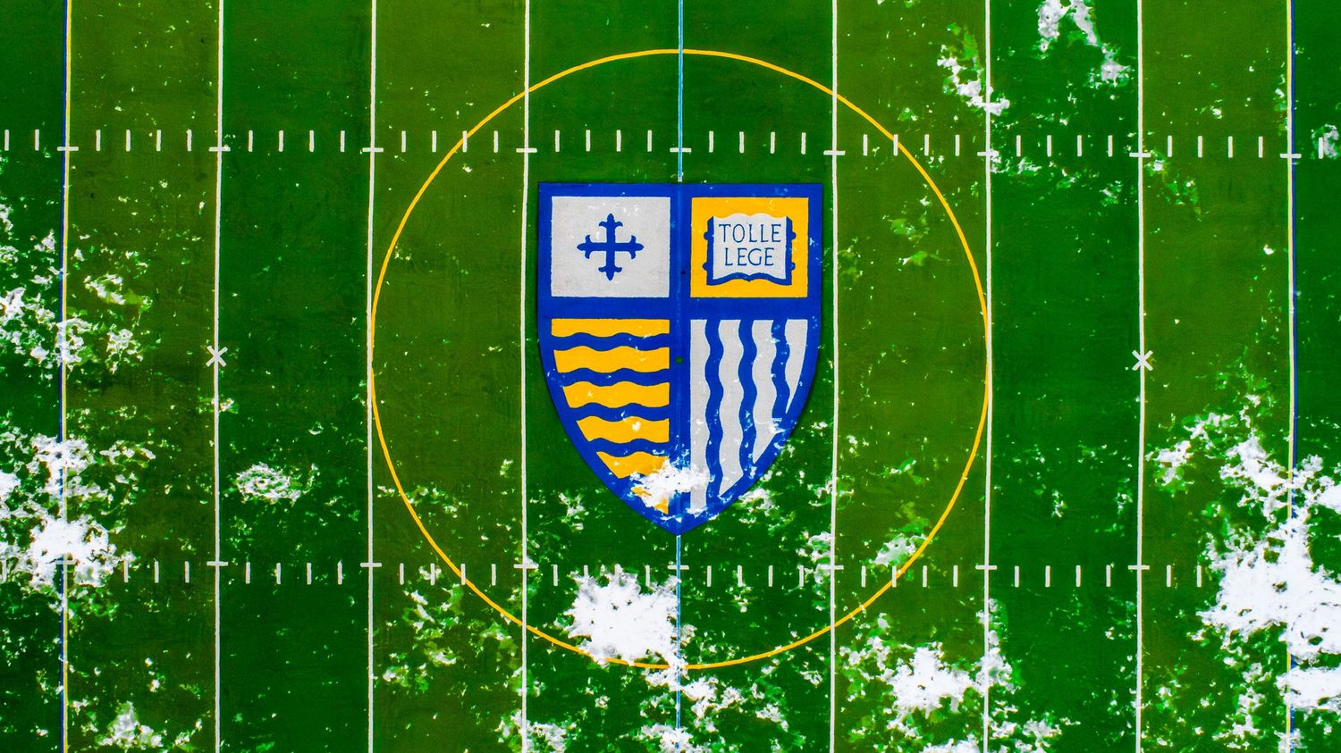 Aerial view of green football field with yard lines and team logos visible.